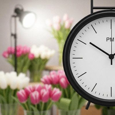 Close-up of a clock showing early afternoon time, with a blurred background of a florist shop or a bouquet of flowers, clean image, no text, no words, no typography
